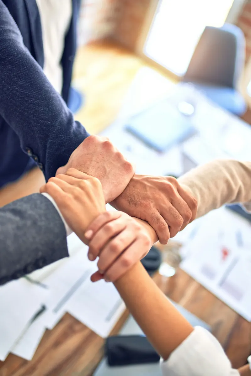 Four colleagues joining hands over a meeting table
